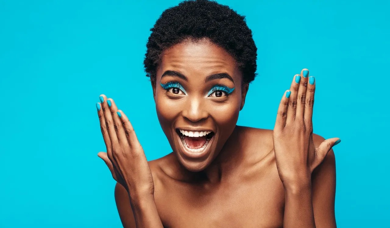 A joyful individual with bold makeup, smiling against a vibrant turquoise background, representing the freedom and empowerment of living single and childfree