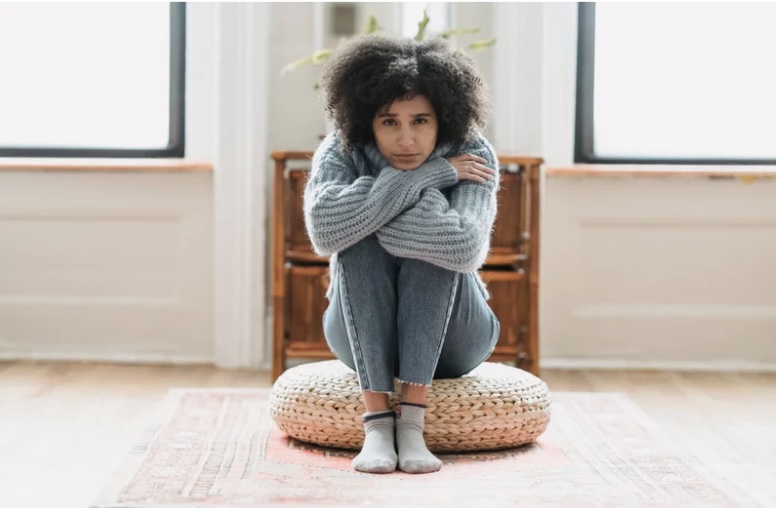 woman sitting on a a cushion with her legs up to her chest and arms wrapped around them