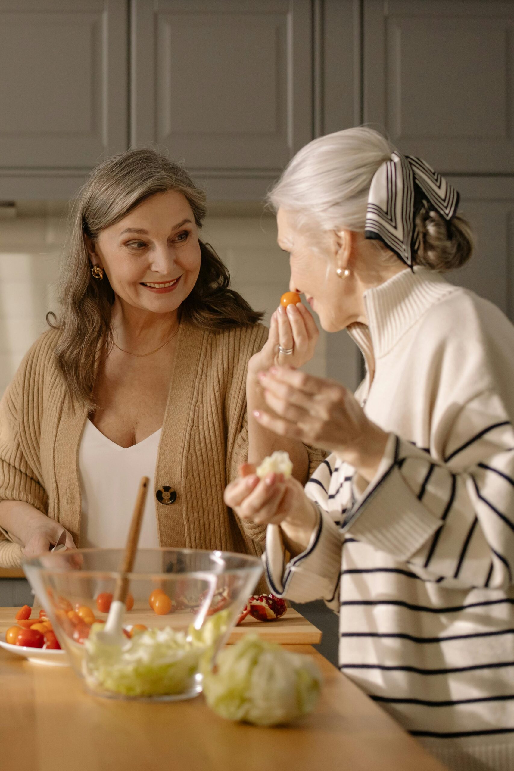 Two women of different generations preparing food together in a kitchen, demonstrating intergenerational friendship and community building for aging without kids